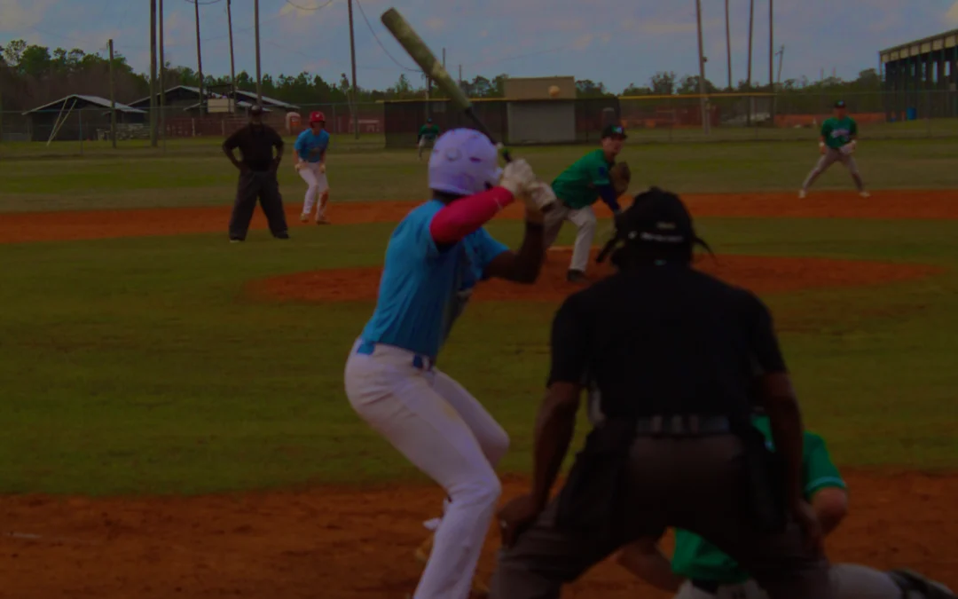 A youth baseball game in progress, featuring players in colorful uniforms on a grass field with cloudy skies in the background